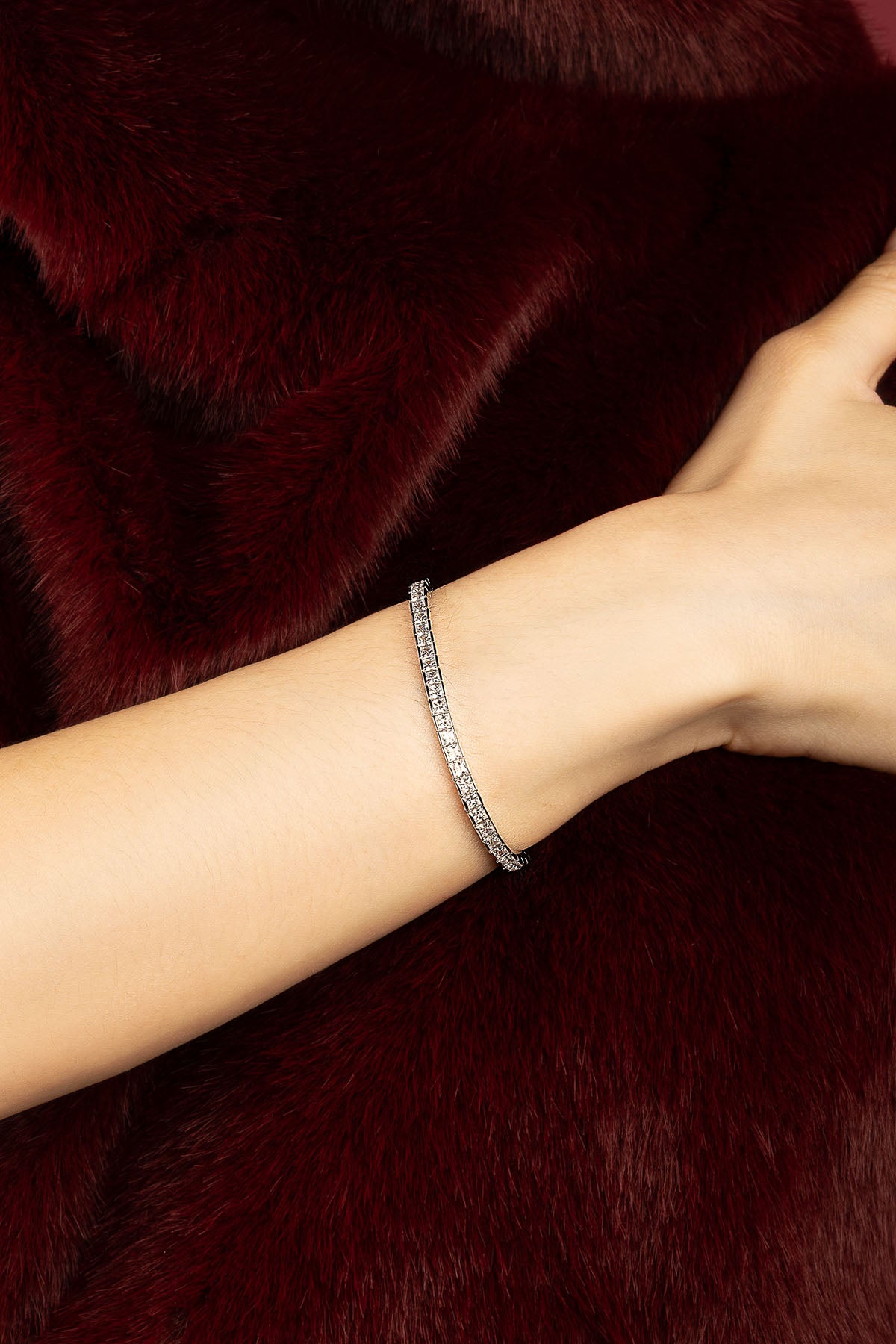Woman wearing APM tennis bracelet, a whisper of shimmer against deep burgundy.