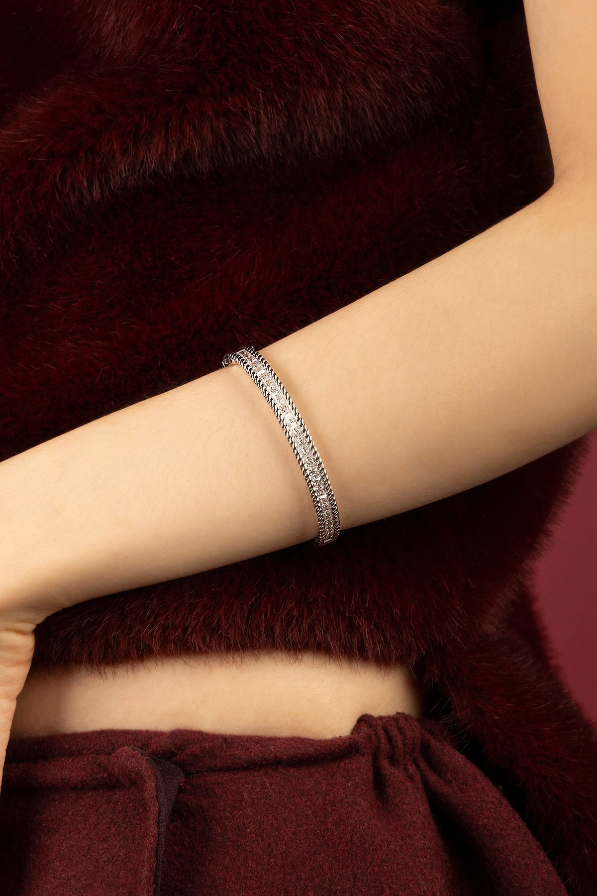 Woman wearing APM Monaco bangle, a shimmer of quiet elegance against burgundy.