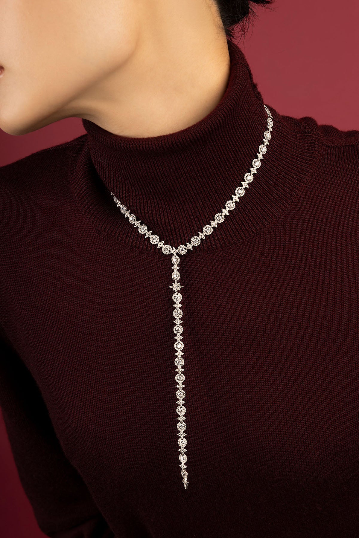 Woman wearing APM lariat necklace, a cascade of starlit elegance against burgundy.