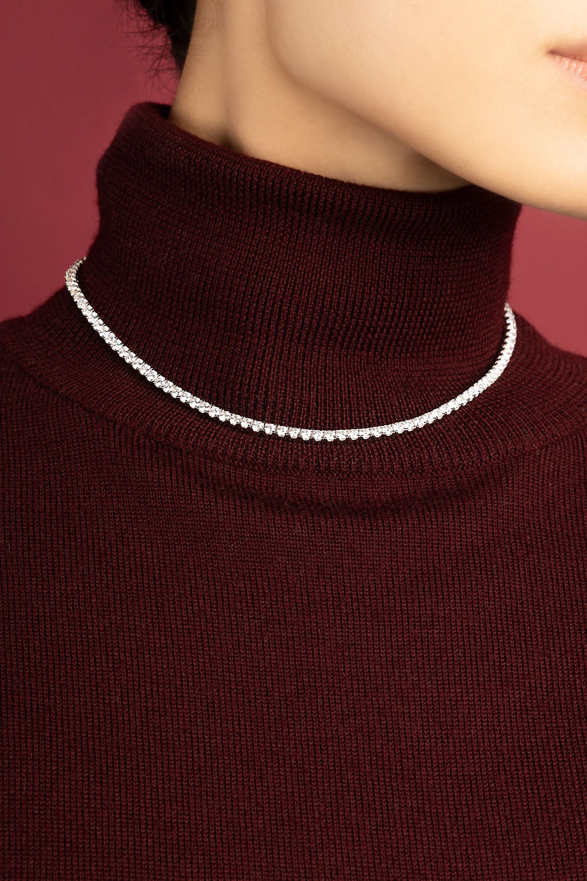 Woman wearing APM tennis necklace, a luminous line against burgundy warmth.