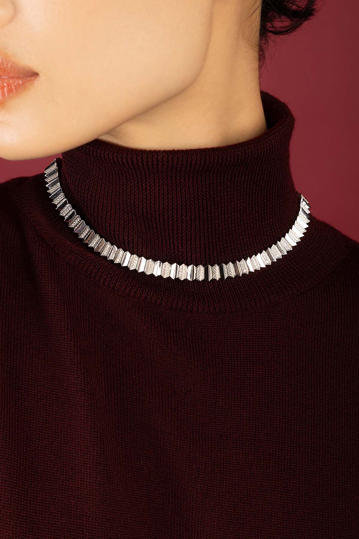Woman wearing APM Monaco necklace, sculpted brilliance framing a rich burgundy allure.