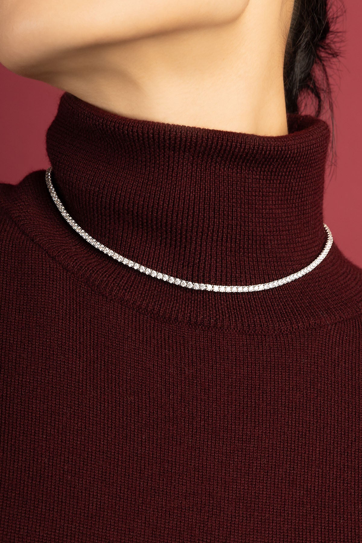 Woman wearing APM tennis necklace, a luminous line gracing burgundy knitwear with quiet elegance.