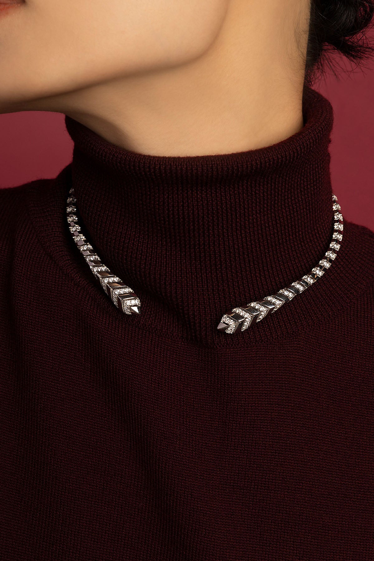Woman wearing APM Monaco necklace, a sleek open silhouette shimmering against burgundy.