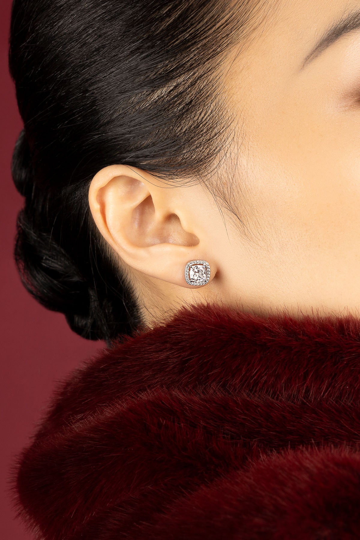 Woman wearing APM Monaco stud earrings, quiet sparkle against crimson elegance.