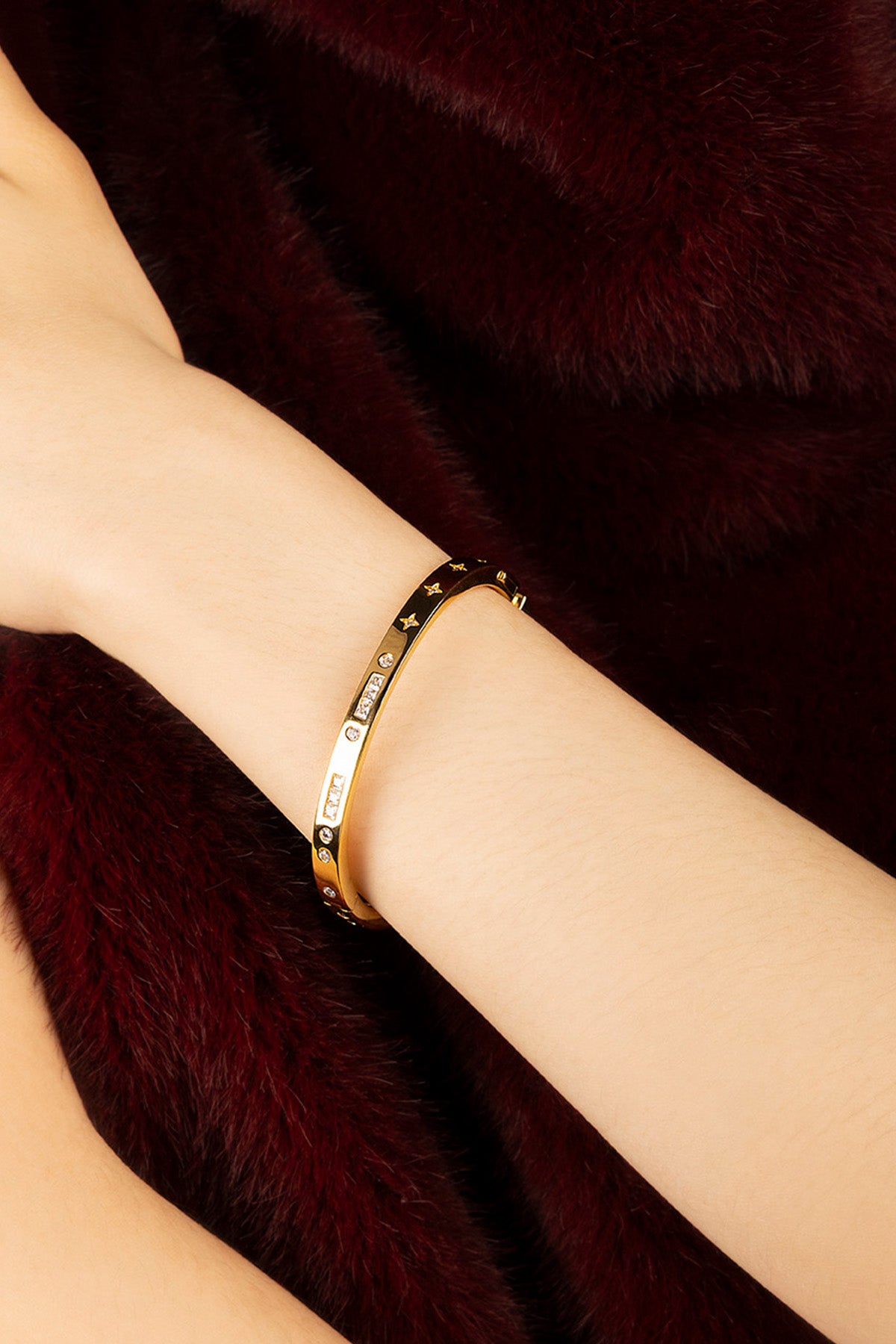 Woman wearing APM Monaco bangle, a golden whisper against velvet richness.