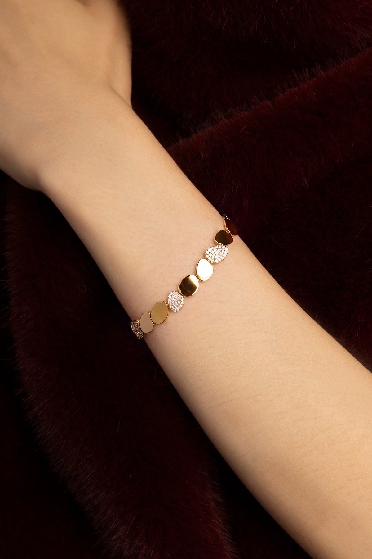 Woman wearing APM bracelet, golden pebbles glowing against plush burgundy.