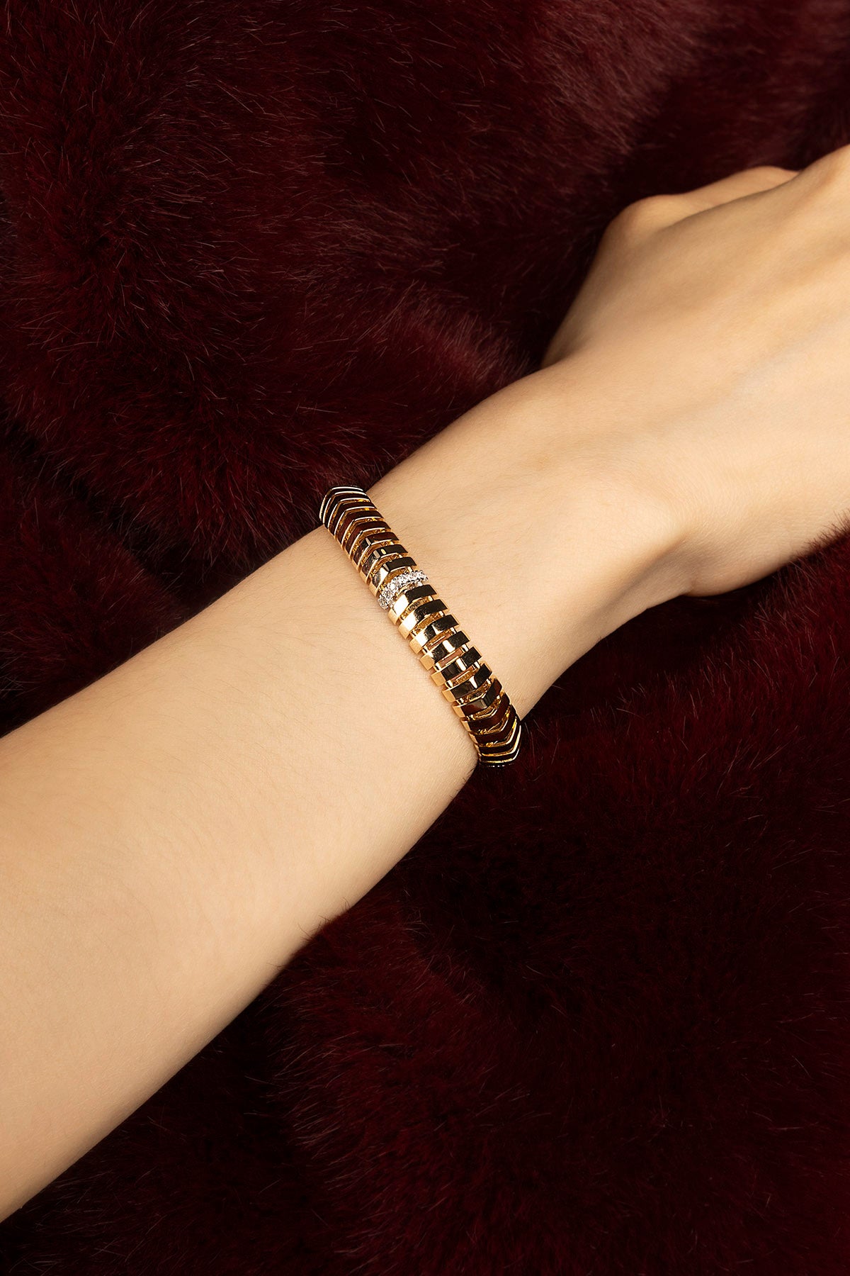Woman wearing APM bracelet, a golden ripple of quiet confidence against velvet.