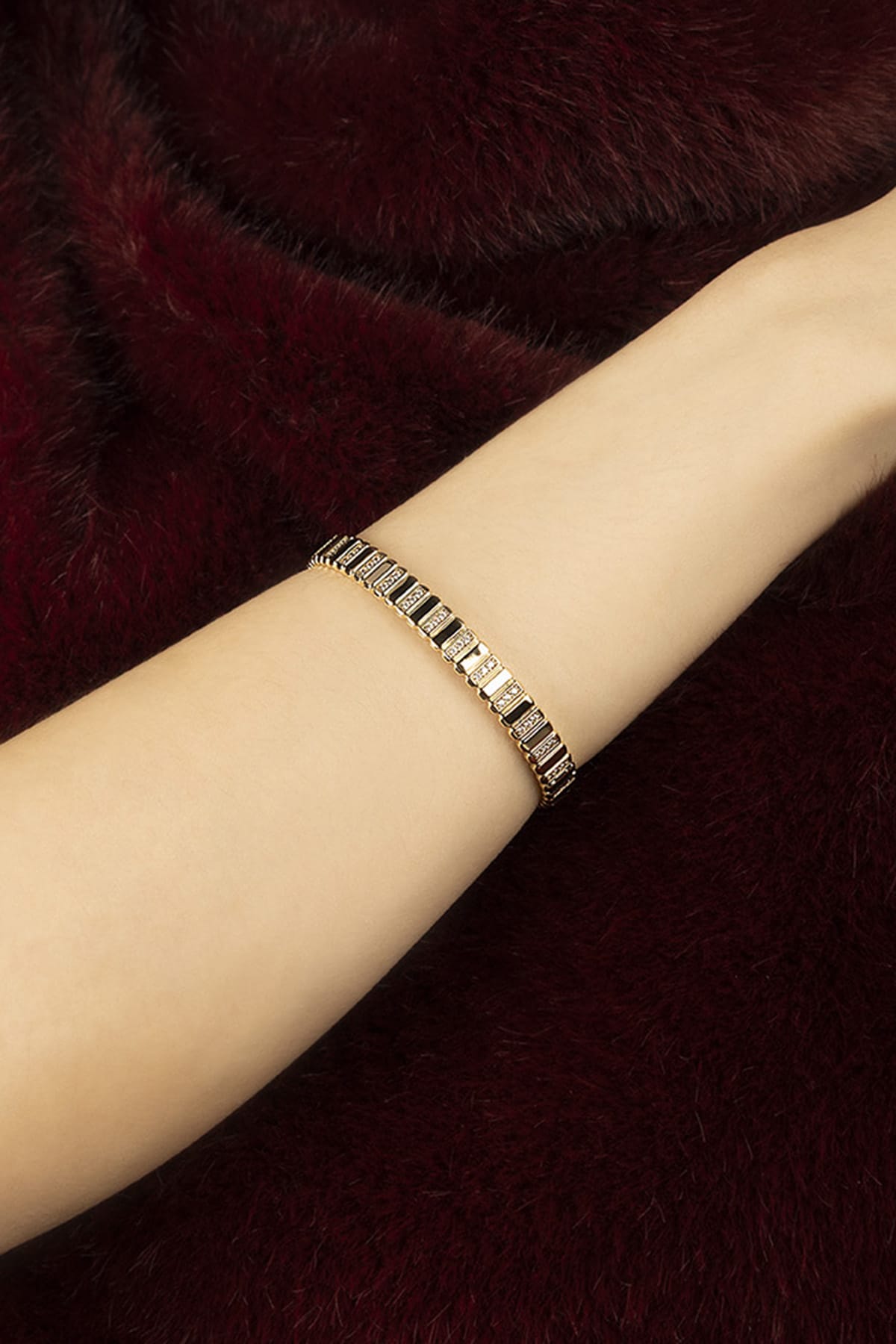 Woman wearing APM bracelet, a golden whisper against velvet warmth.