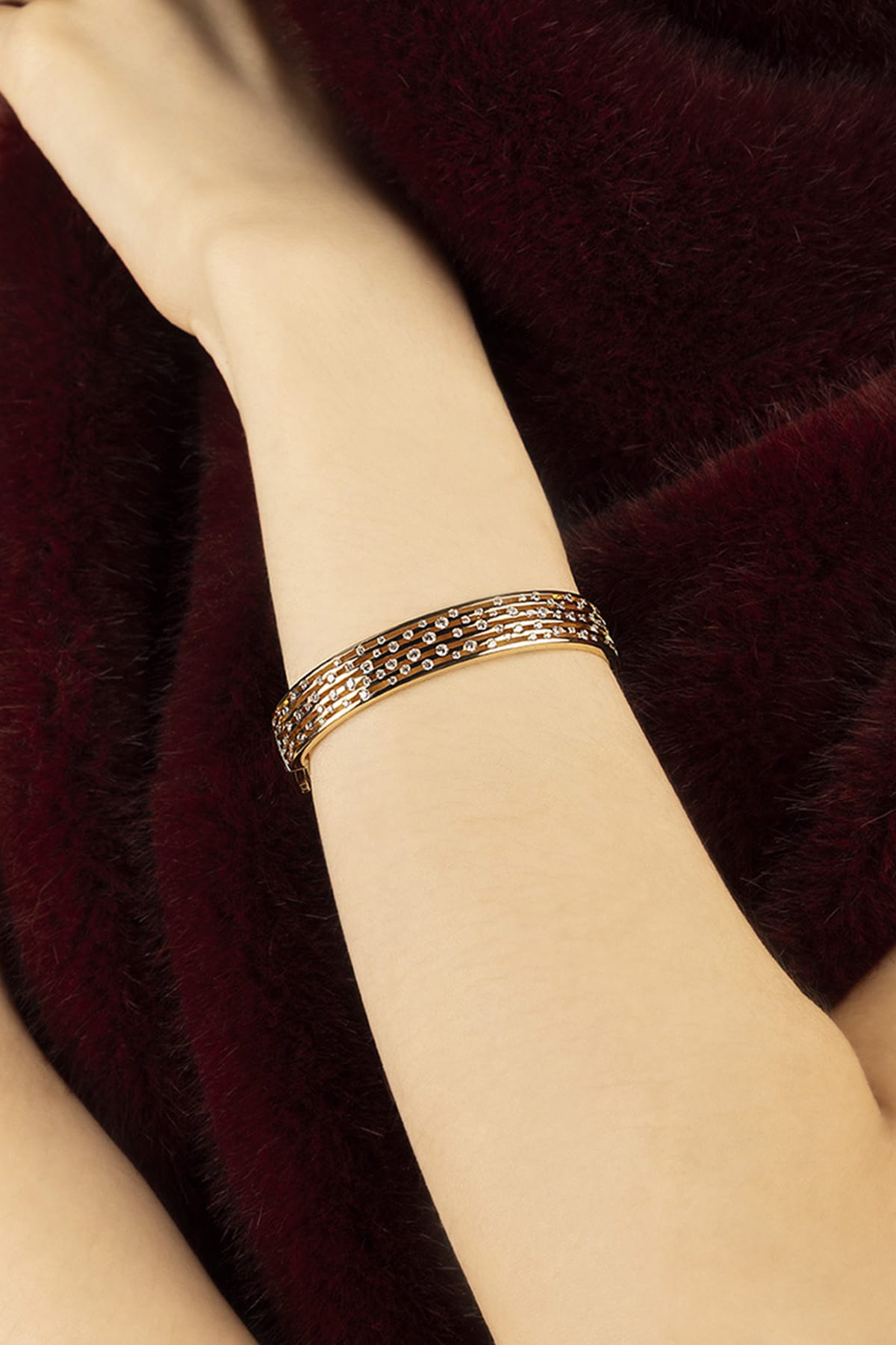 Woman wearing APM Monaco bracelet, a shimmering wrist statement against velvety burgundy.