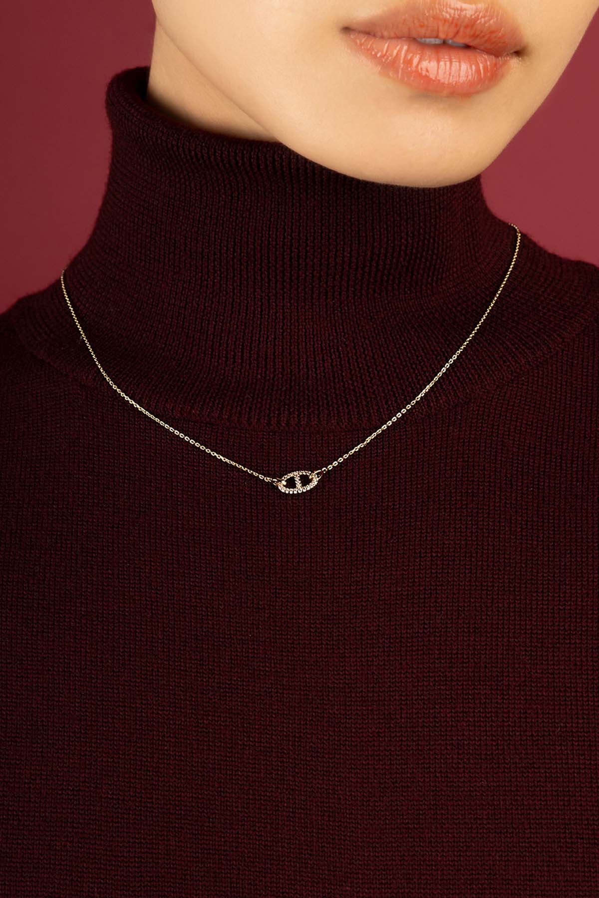 Woman wearing APM Morse Necklace, a delicate glow against burgundy warmth.