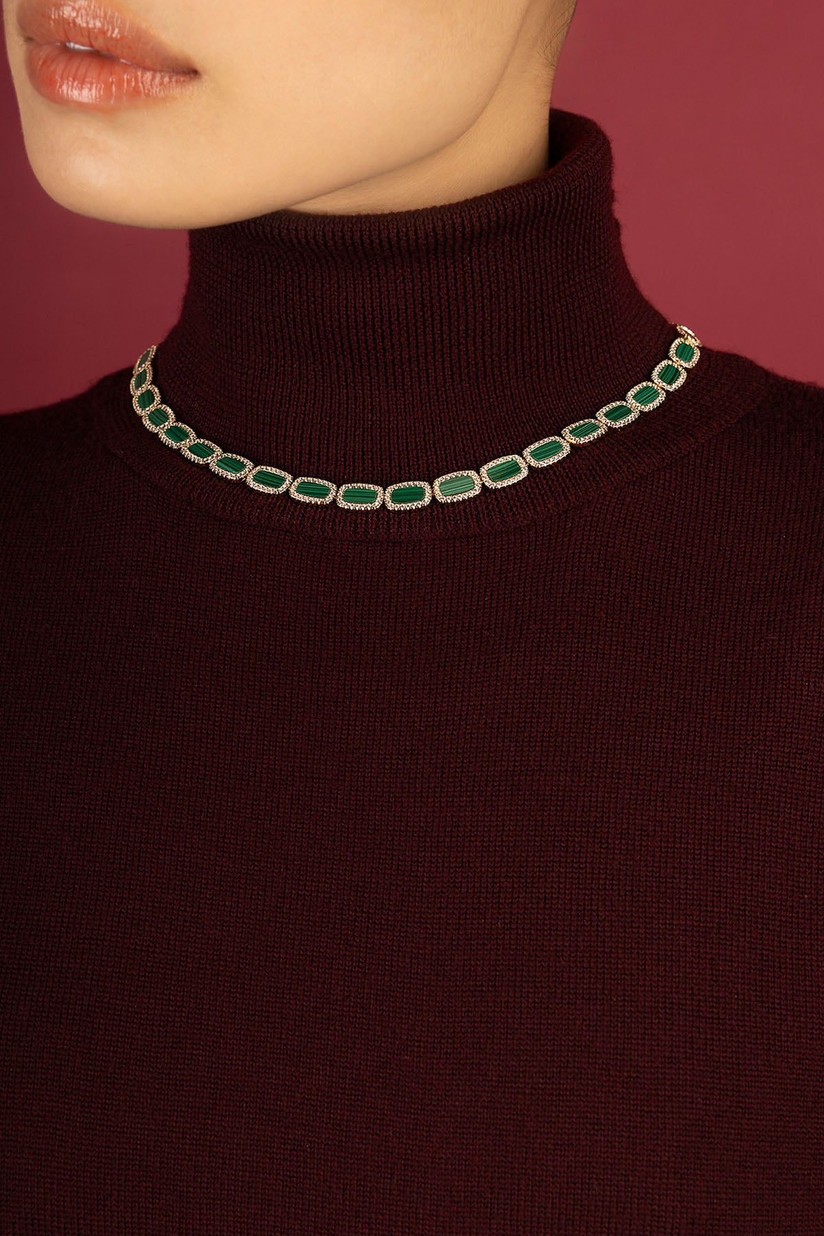 Woman wearing APM Monaco necklace, emerald green hues glowing against burgundy elegance.