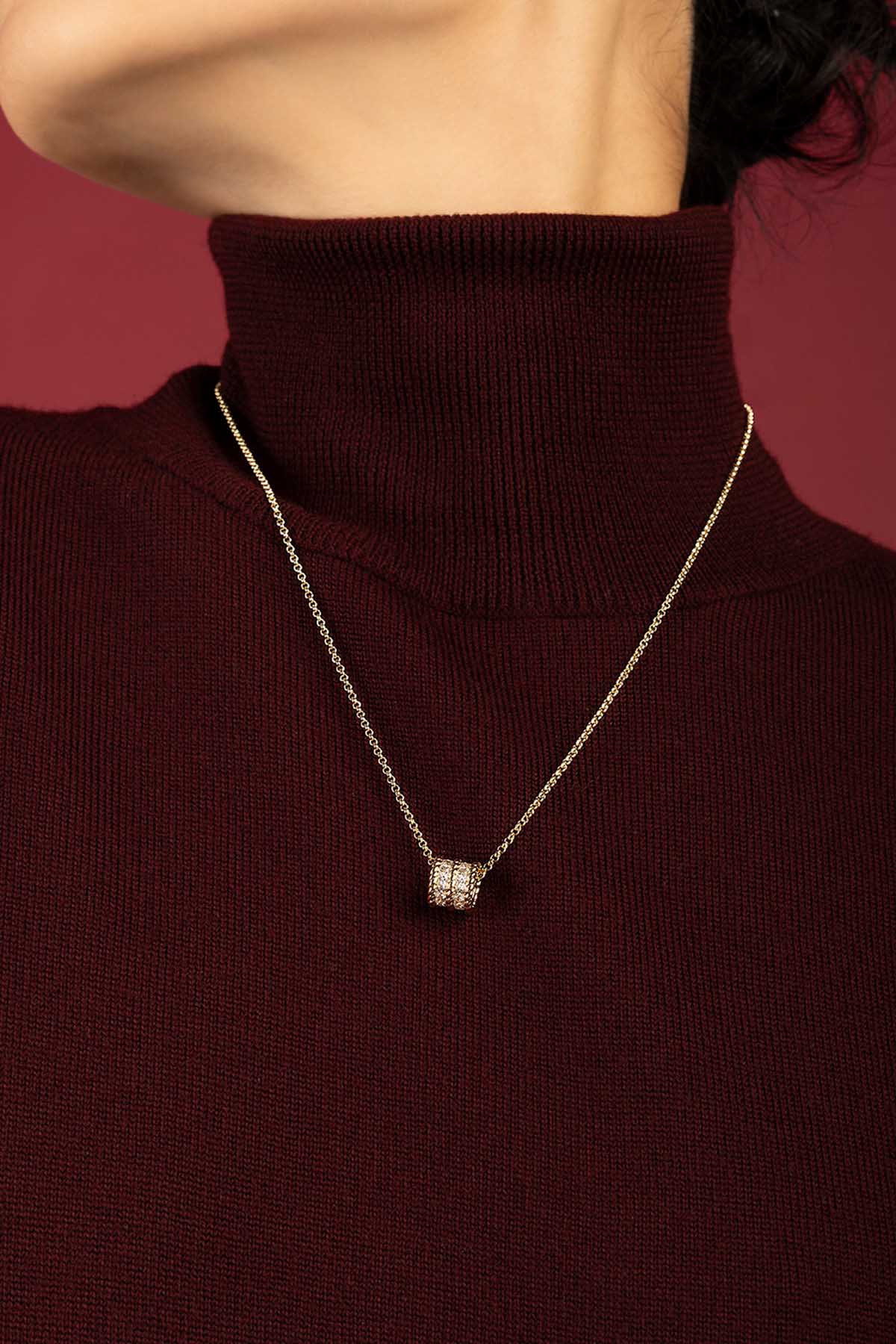 Woman wearing APM Monaco pendant necklace, a golden whisper on burgundy warmth.