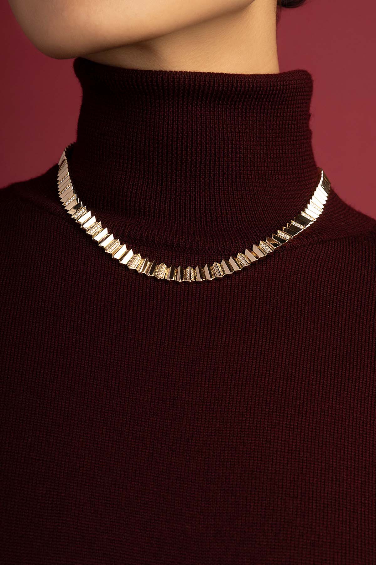 Woman wearing APM Monaco necklace, a sculpted glow against burgundy warmth.