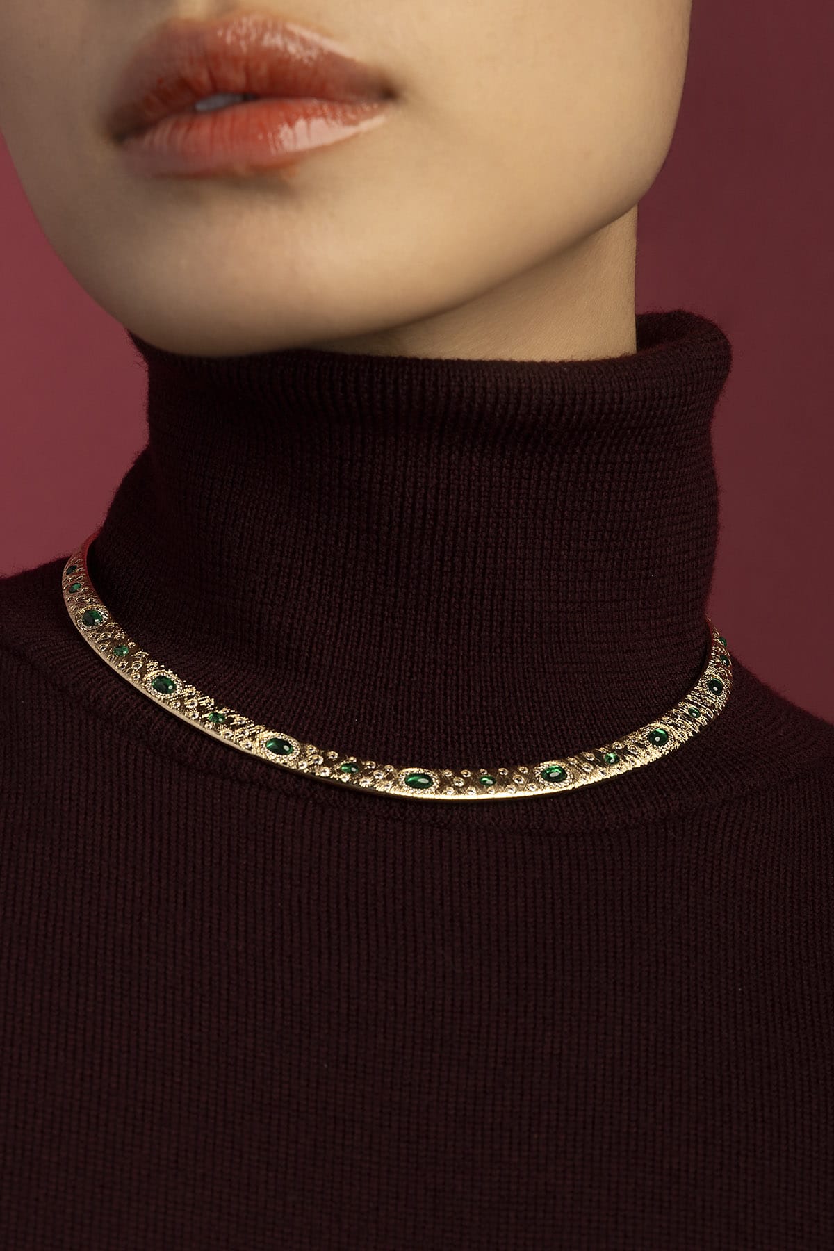 Woman wearing APM Monaco necklace, emerald hues glowing against burgundy warmth.