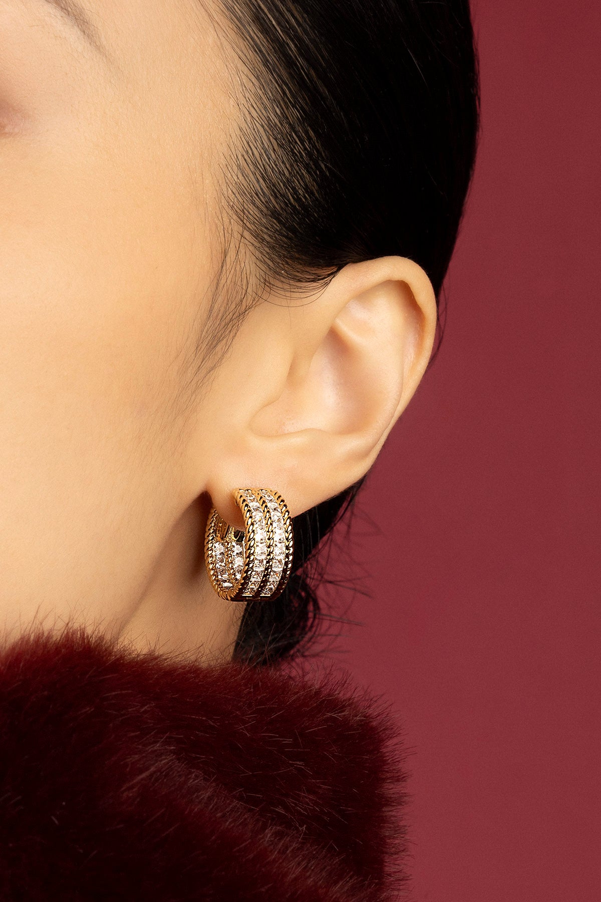 Woman wearing APM hoop earrings, a golden glow against burgundy warmth.