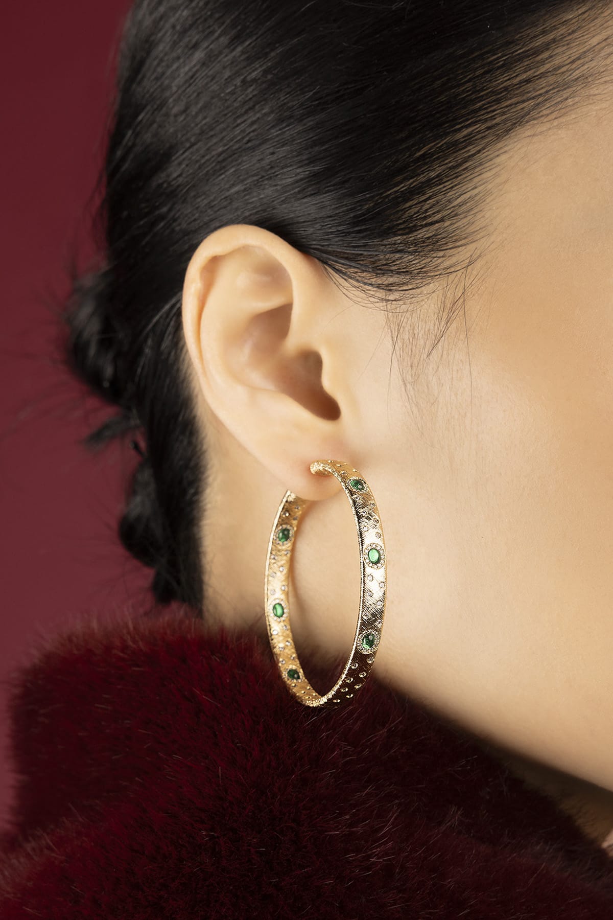 Woman wearing APM Monaco hoop earrings, golden allure touched with emerald green sparks.