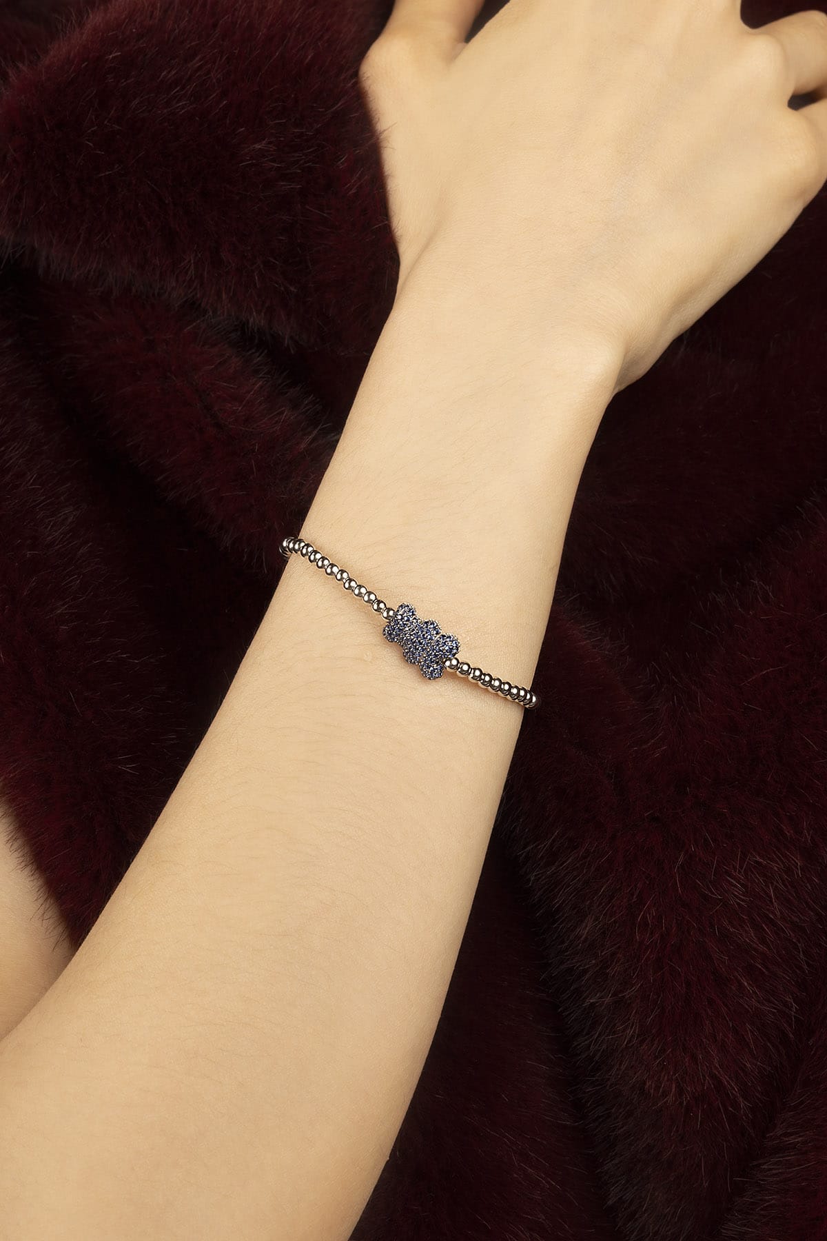 Woman wearing APM beaded bracelet, a delicate bloom of blue against burgundy fur.