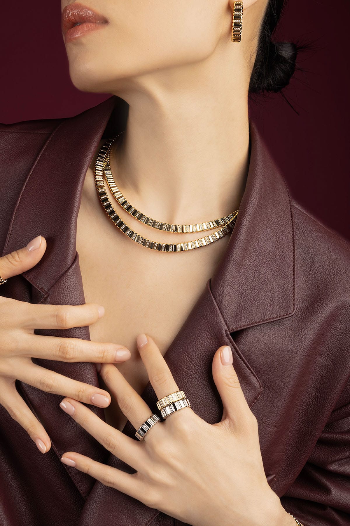 Woman wearing APM Monaco layered necklaces, rings and earrings, radiant in golden sophistication.