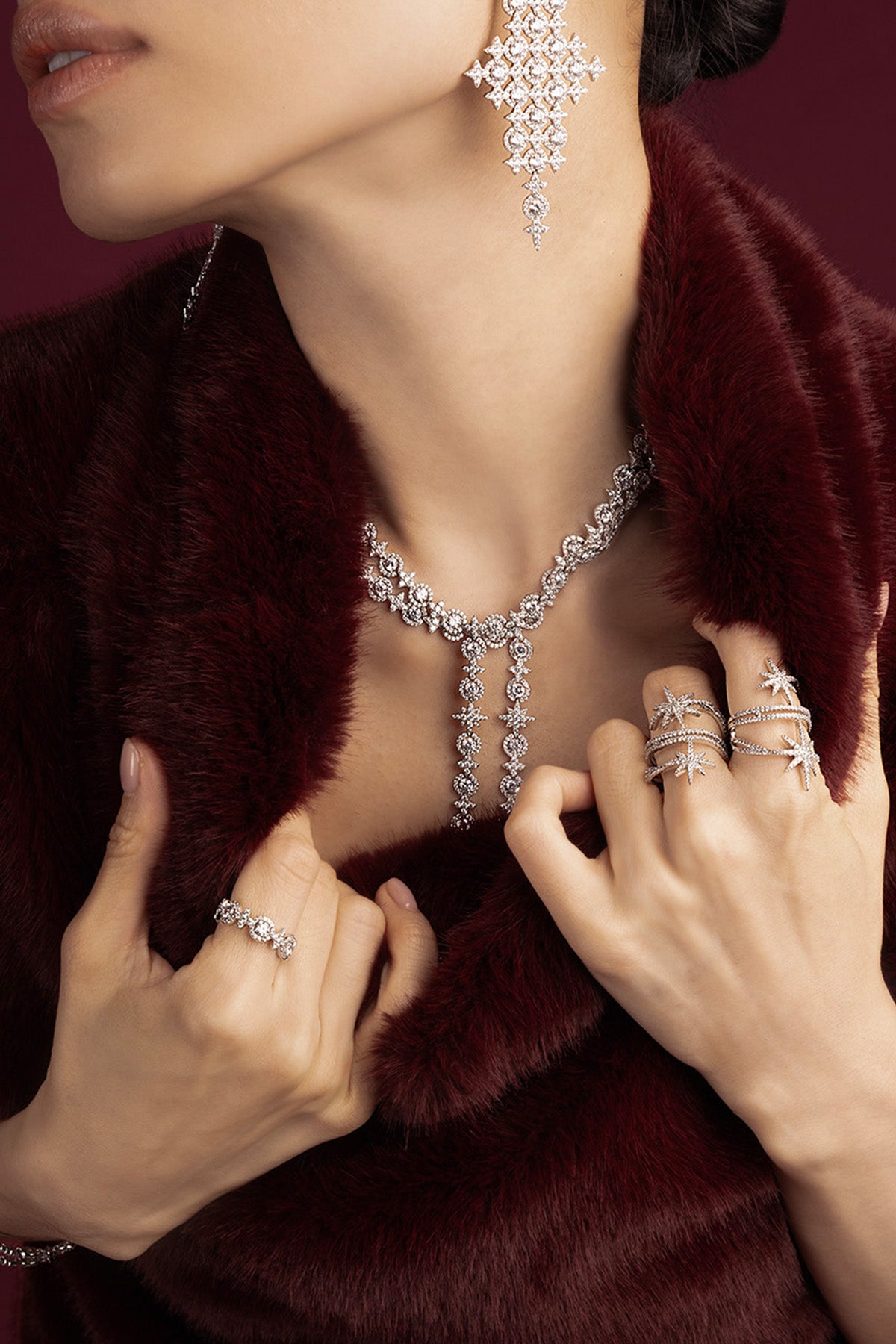 Woman wearing APM necklace, earrings and rings, radiant sparkle against deep burgundy elegance.