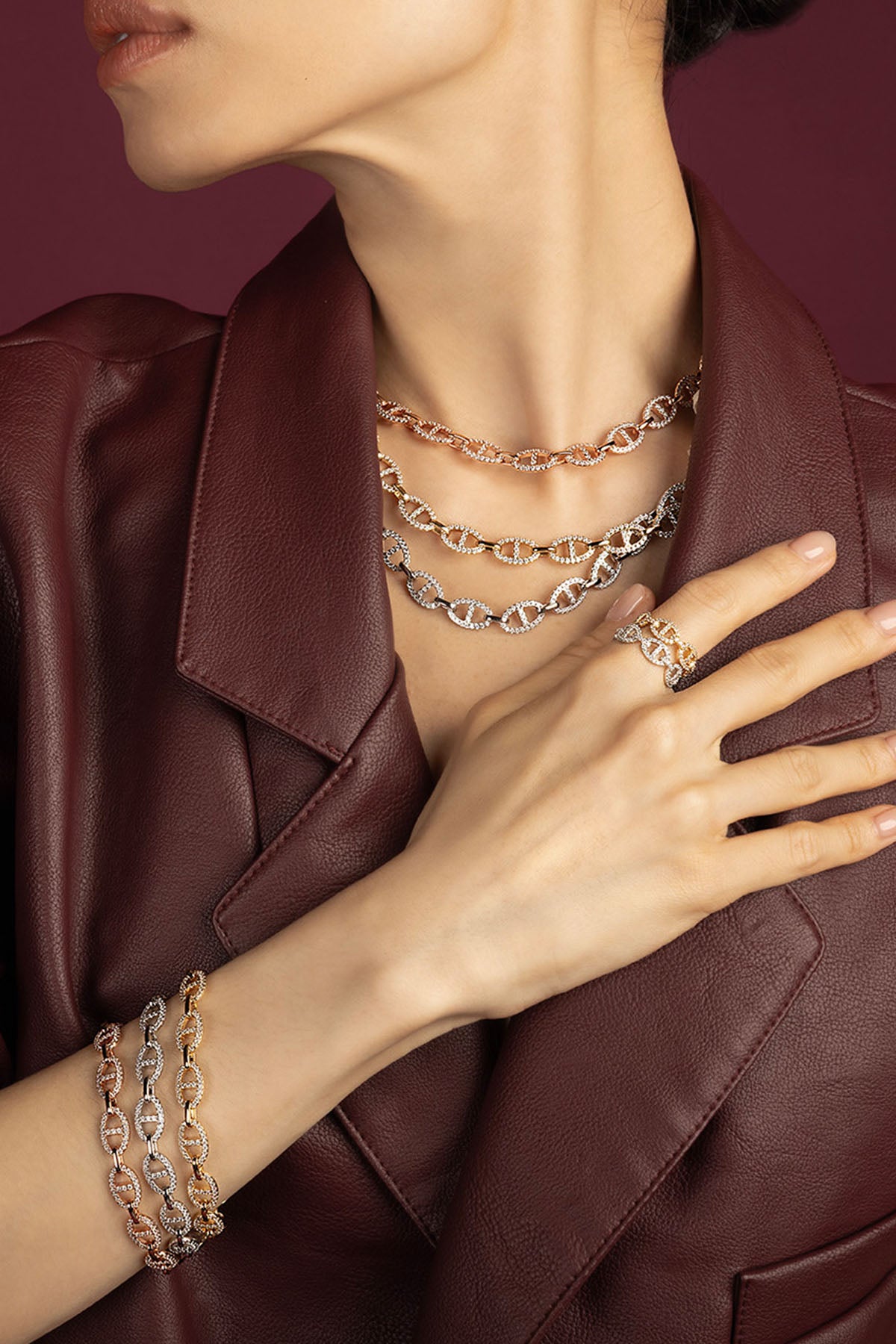 Woman wearing APM Monaco chain necklaces, bracelets and ring, layered bold elegance in burgundy leather.