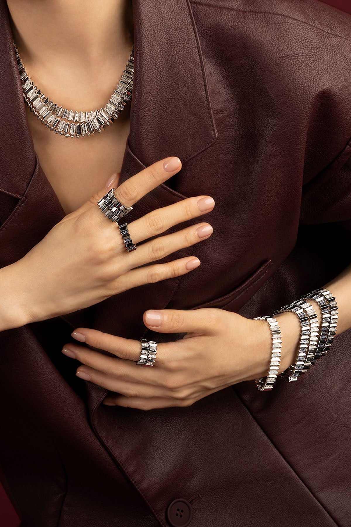 Woman wearing APM Morse jewelry set, bold rhodium finish against deep burgundy elegance.