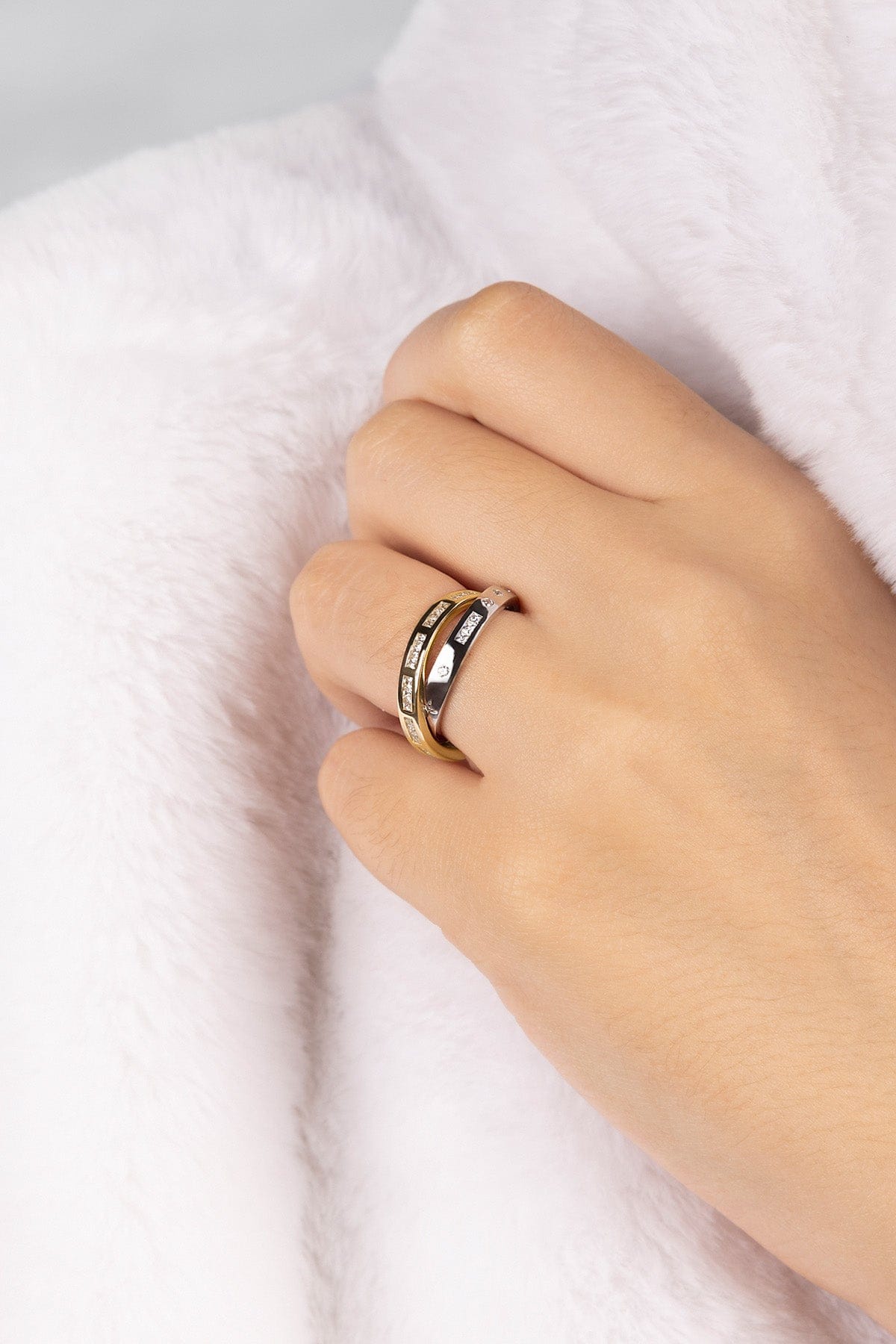 Hand wearing a gold and silver ring on a white fabric background