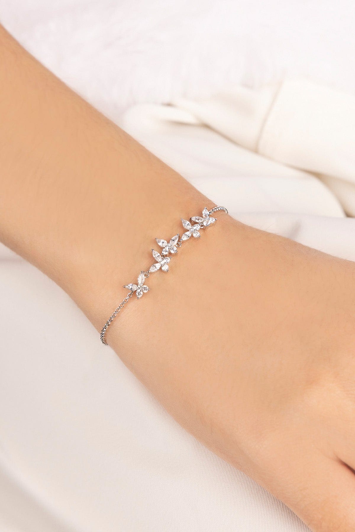 Silver bracelet with butterflies design on a wrist against a white background