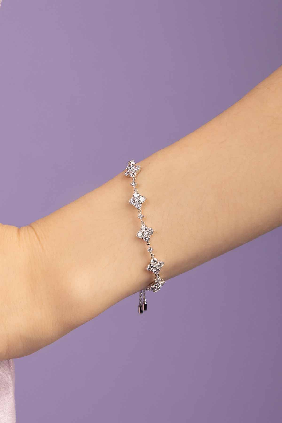 Silver-tone bracelet with floral charms on a person's wrist against a purple background