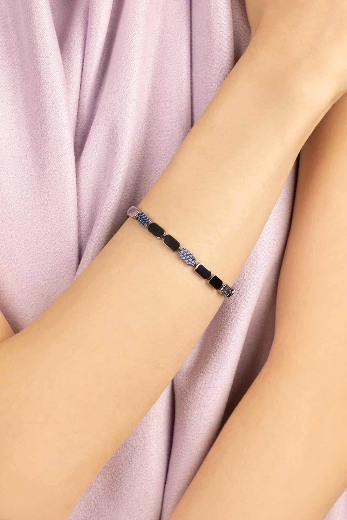 Bracelet with blue and silver on a wrist against a soft pink fabric background