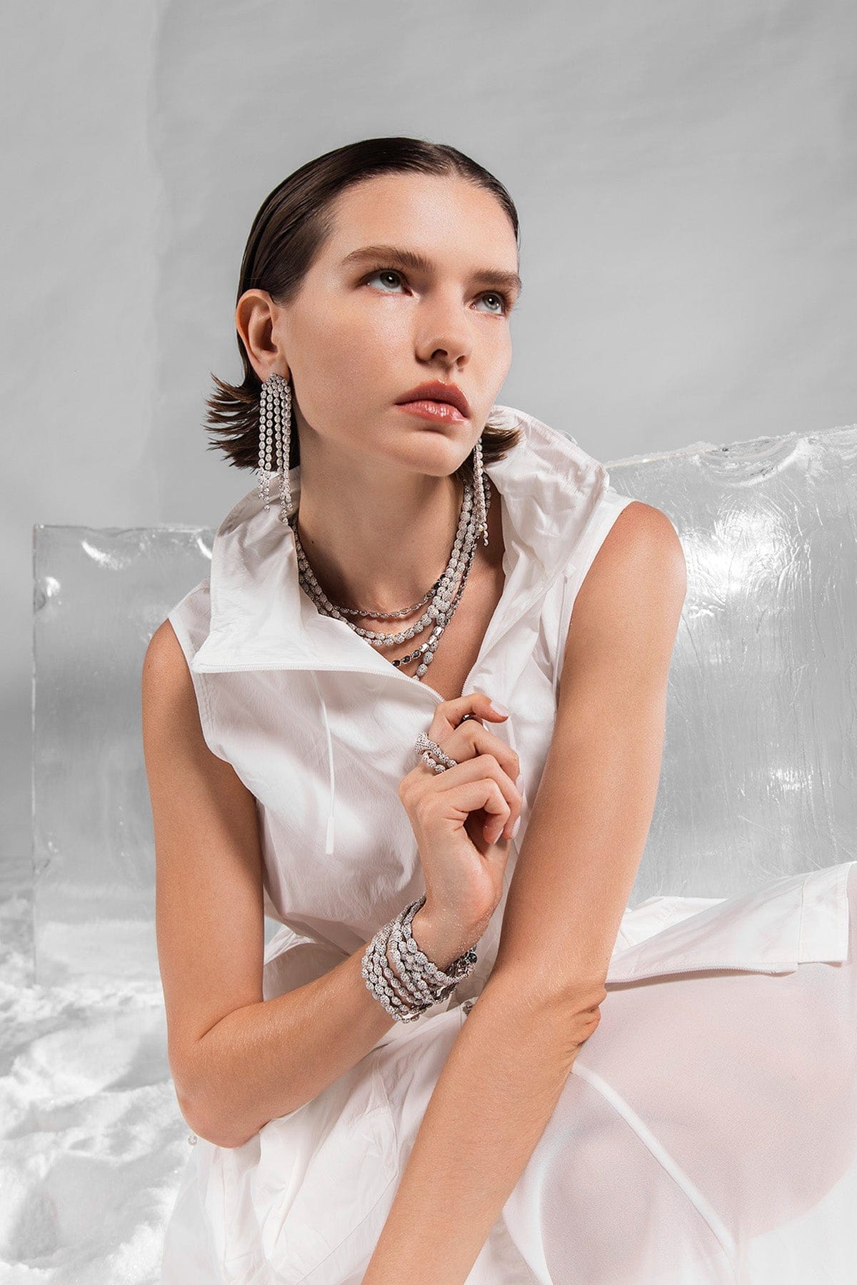 Woman in a white dress with APM MONACO pave jewelry against a gray background
