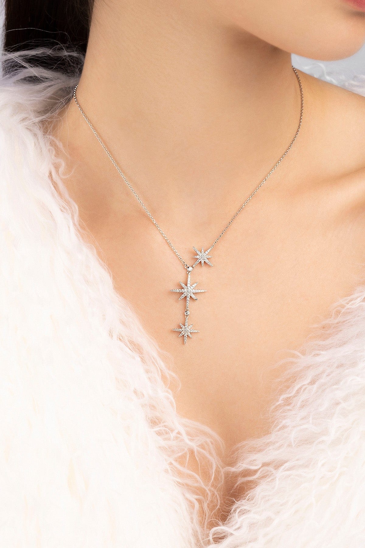 Silver necklace with star-shaped pendants on a person wearing a white fur garment.