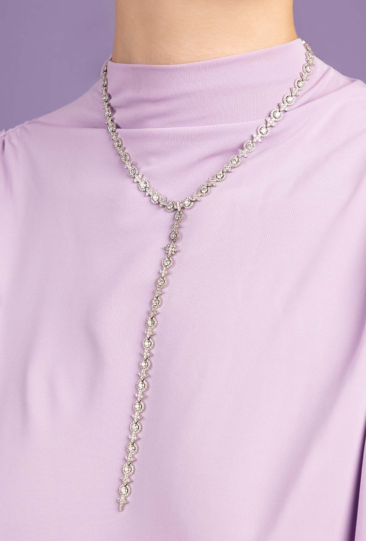Silver chain necklace on a person wearing a light purple top against a light purple background
