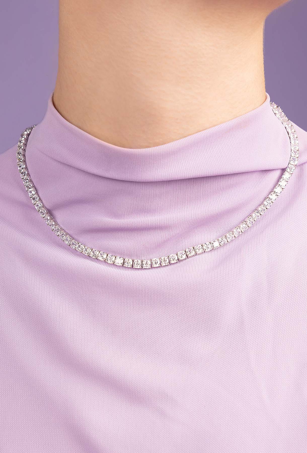 Close-up of a person wearing a lavender dress with a sparkling necklace against a purple background