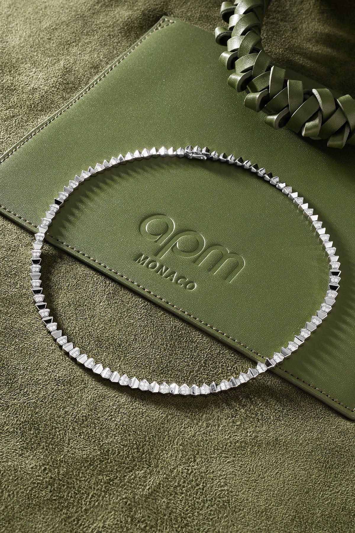 Green handbag with and a silver necklace on a textured green surface.