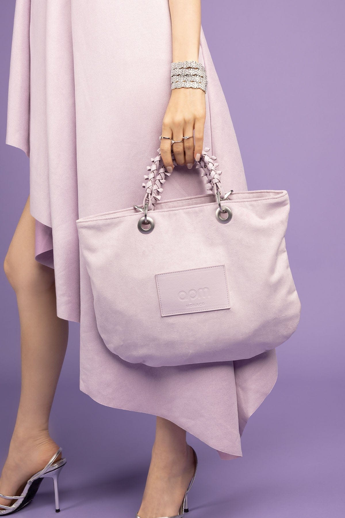 Person holding a light purple handbag with a visible APM Monaco logo against a purple background