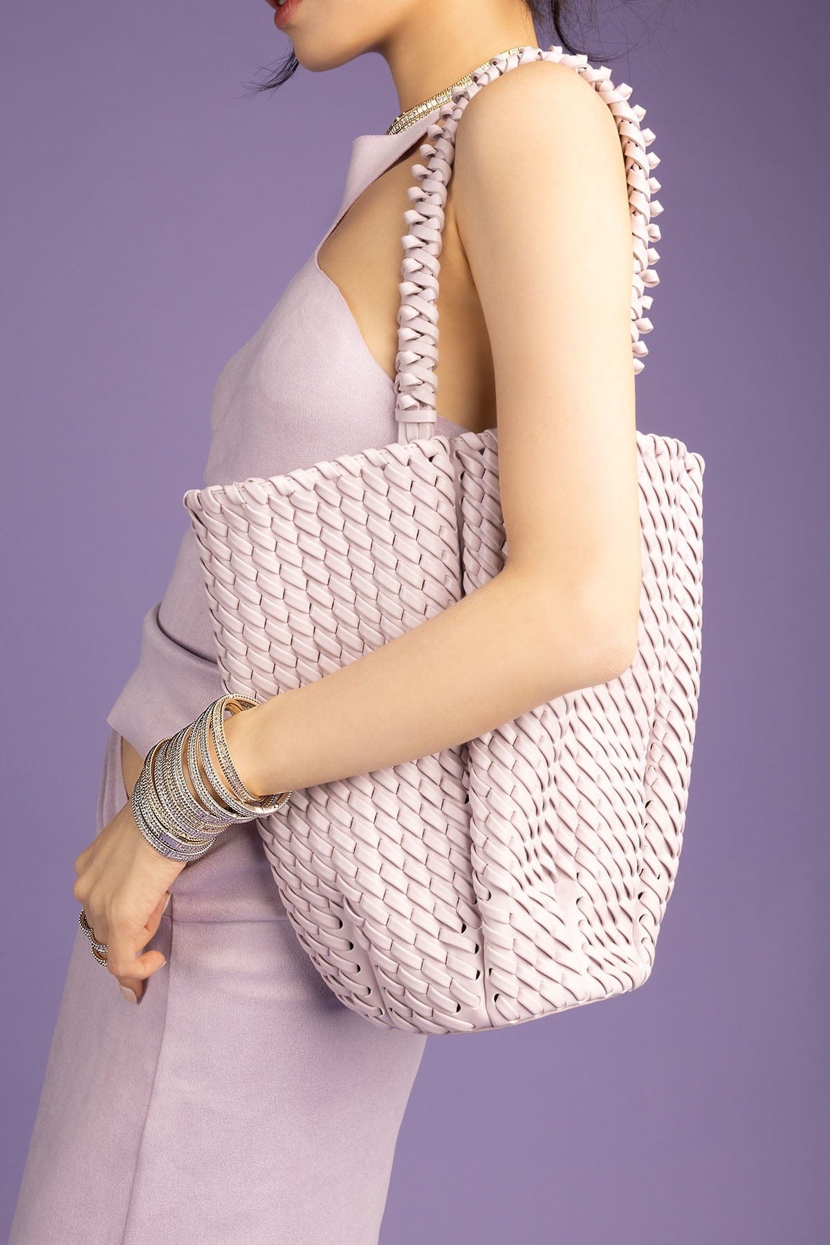 Person holding a woven handbag against a purple background