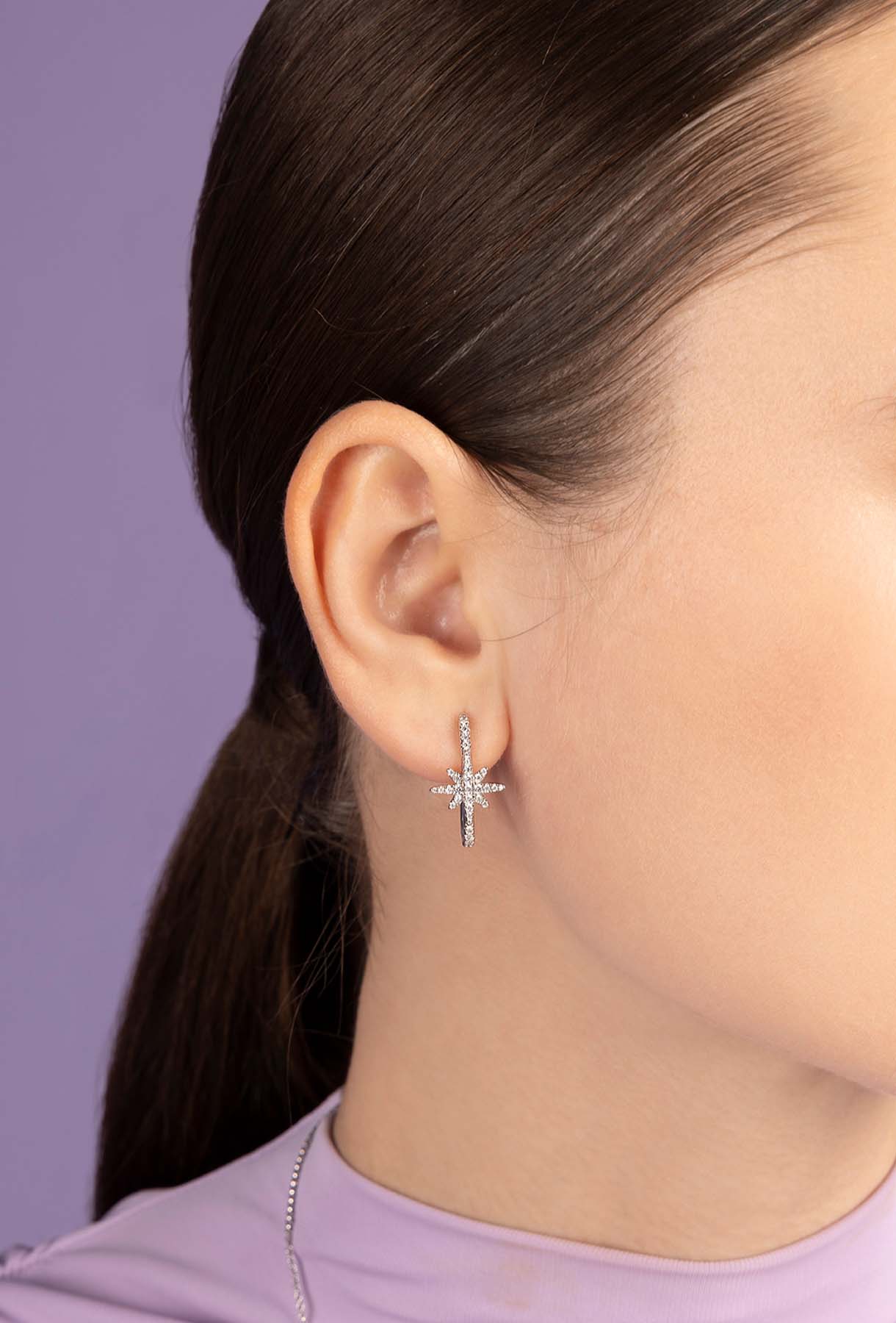 Close-up of a person wearing a silver star earring against a purple background
