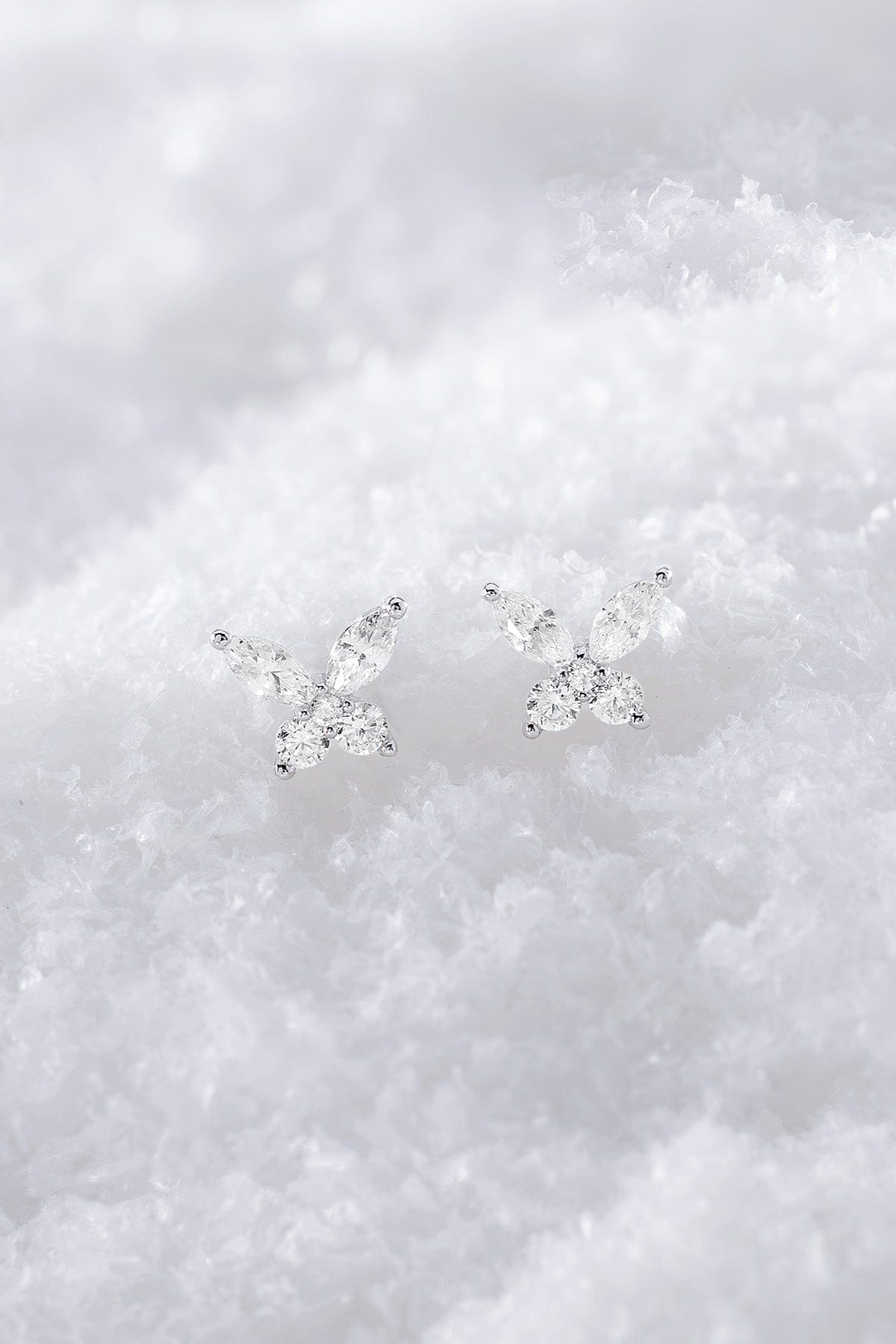 Pair of silver stud earrings with butterfly design from APM MONACO on a snowy surface