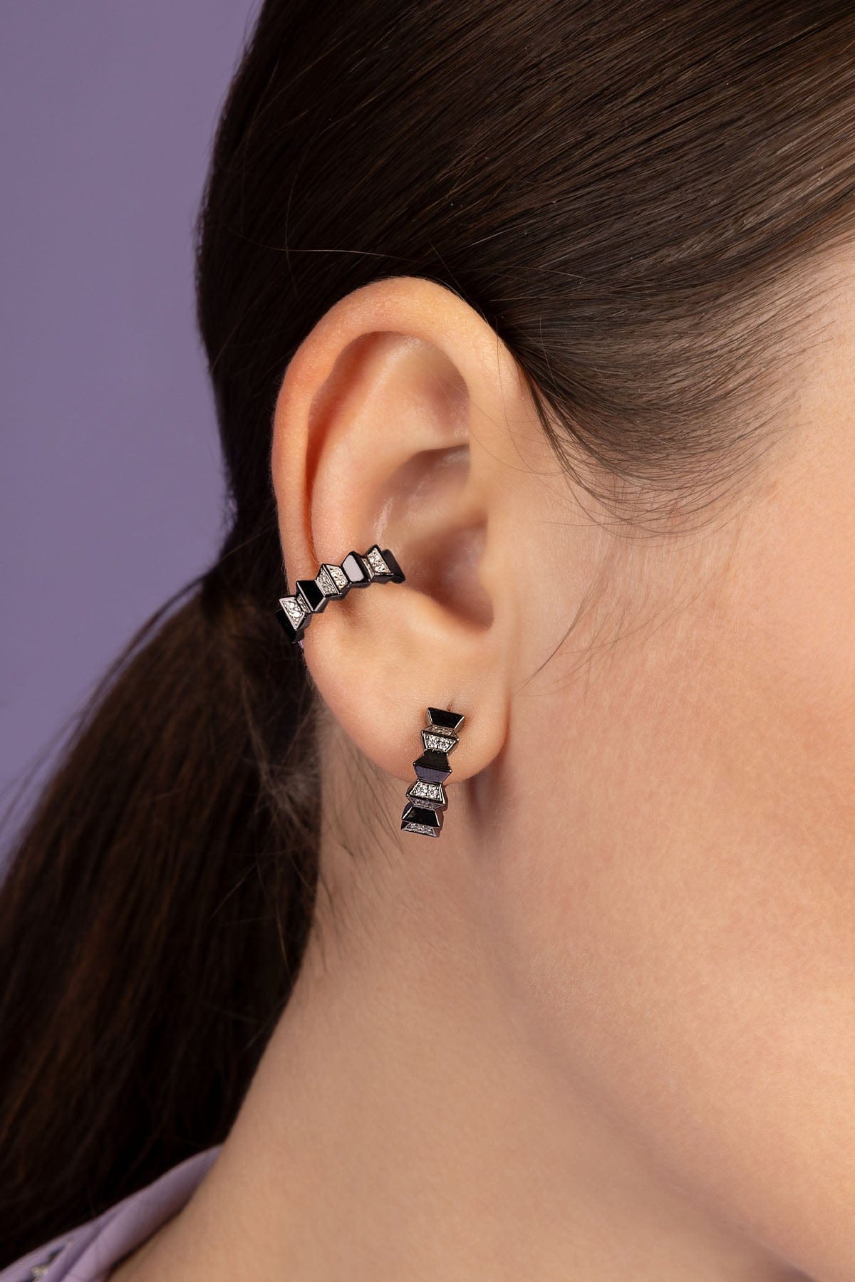 A silver geometric earring worn on a model's ear