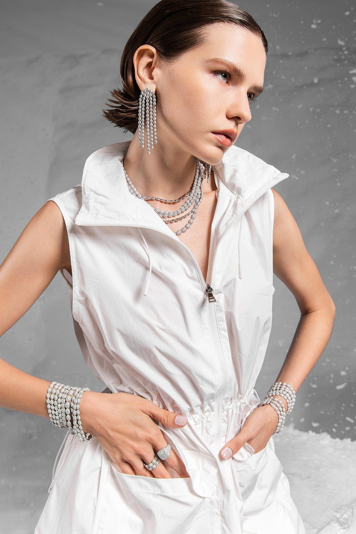 Model wearing a white sleeveless top with APM MONACO pave cascade jewelry against a gray background