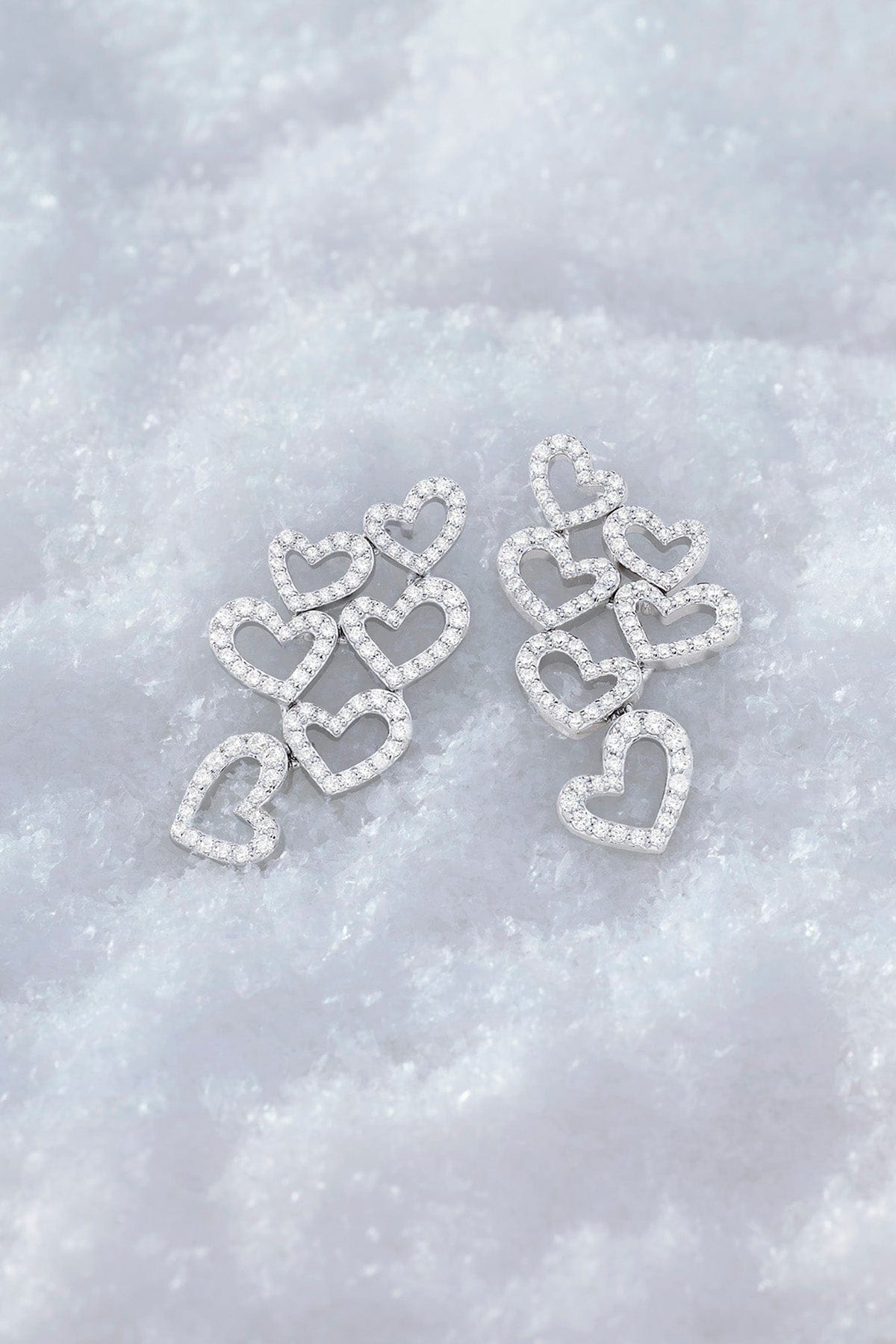 APM MONACO heart-shaped earrings in silver on a textured white surface