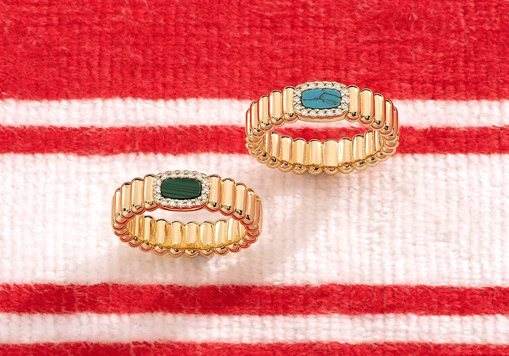 Two APM Yellow rings with green and blue stones on a red and white striped fabric background