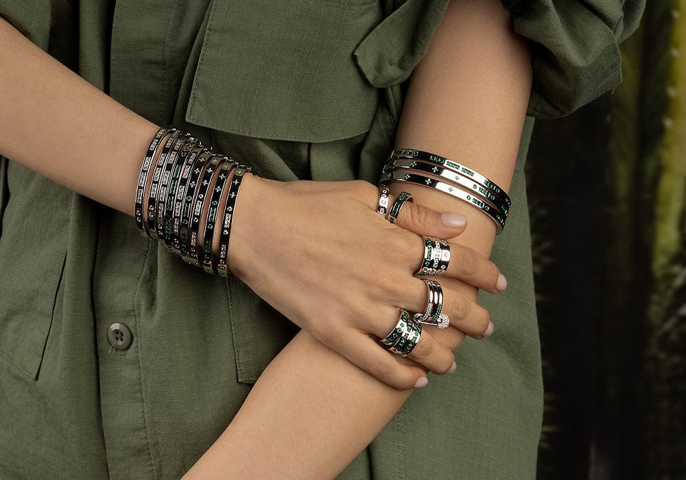 Close-up of hands wearing multiple bracelets and rings on a green background
