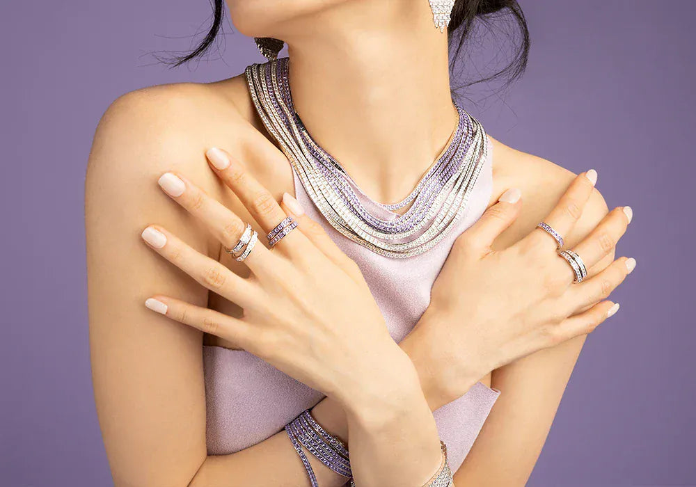 Woman wearing multiple pieces of APM MONACO jewelry including necklaces, rings, and earrings on a purple background