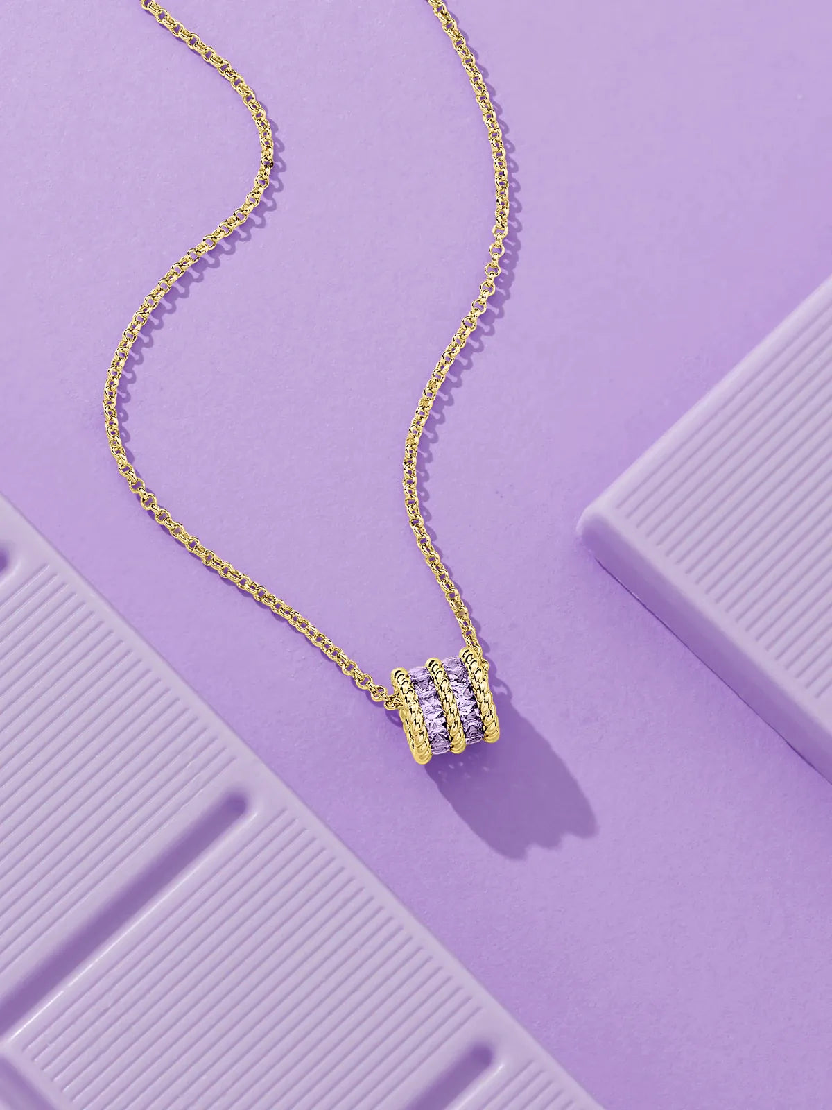 APM Monaco Torsade Gold necklace with lilac stones on a purple surface