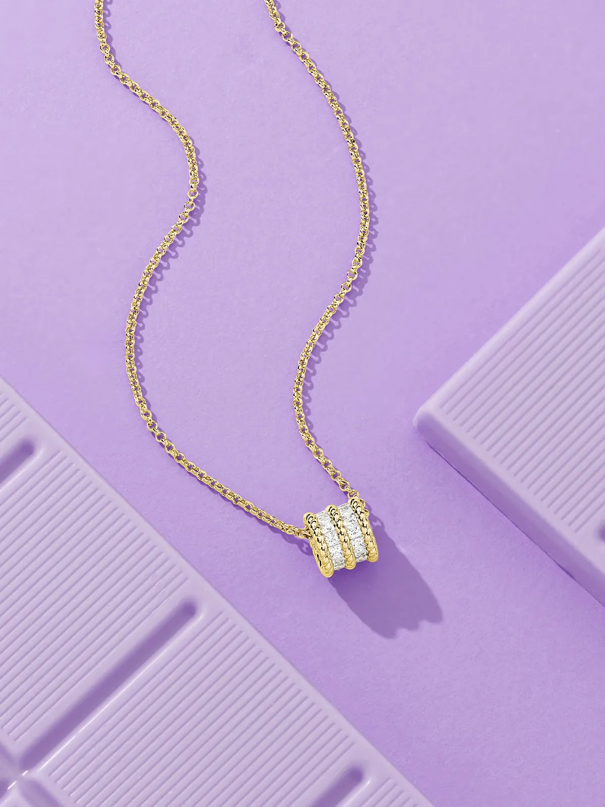 APM Monaco yellow Gold torsade necklace with a beaded pendant on a purple textured surface