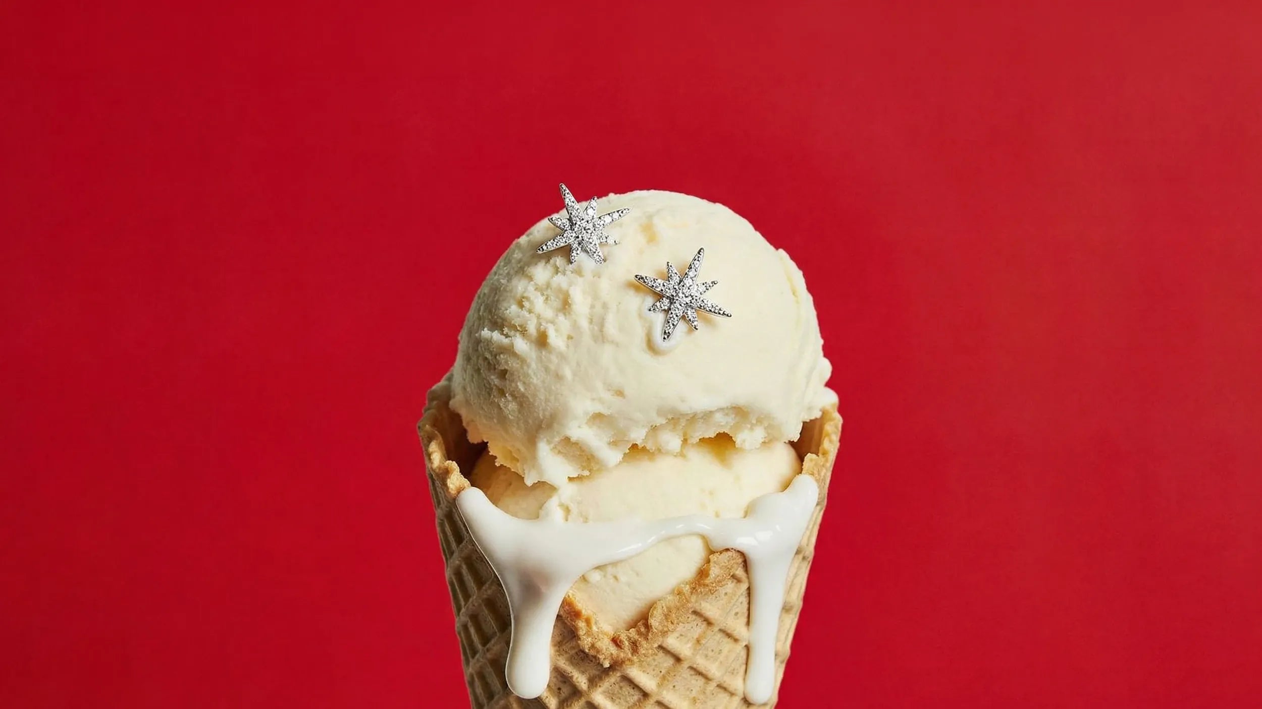 Ice cream cone with a scoop of vanilla ice cream and star-shaped APM MONACO jewelry on a red background
