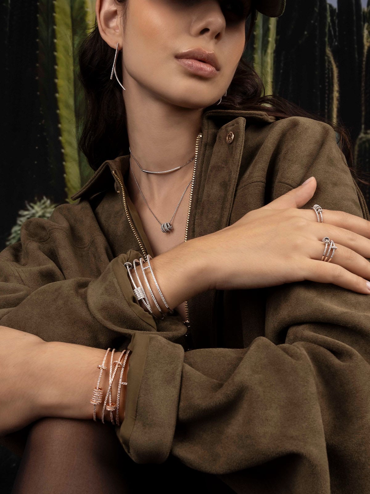 Woman wearing a brown jacket with apm jewelry, including rings and bracelets, against a dark background.