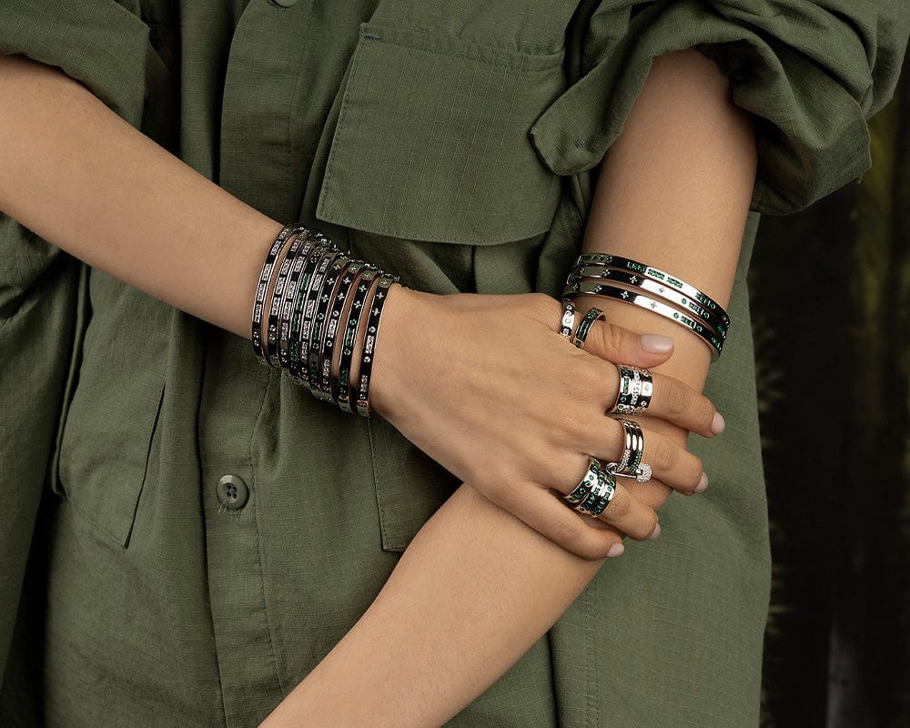 Close-up of a person wearing multiple APM MONACO bracelets and rings on an olive green shirt background