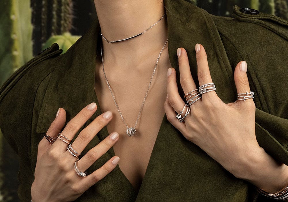Person wearing multiple rings on fingers and a necklace, with a green jacket.